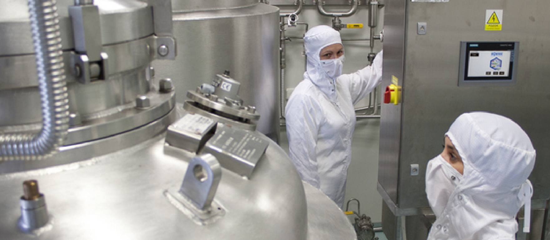 Two people in protective suits stand by steel tanks